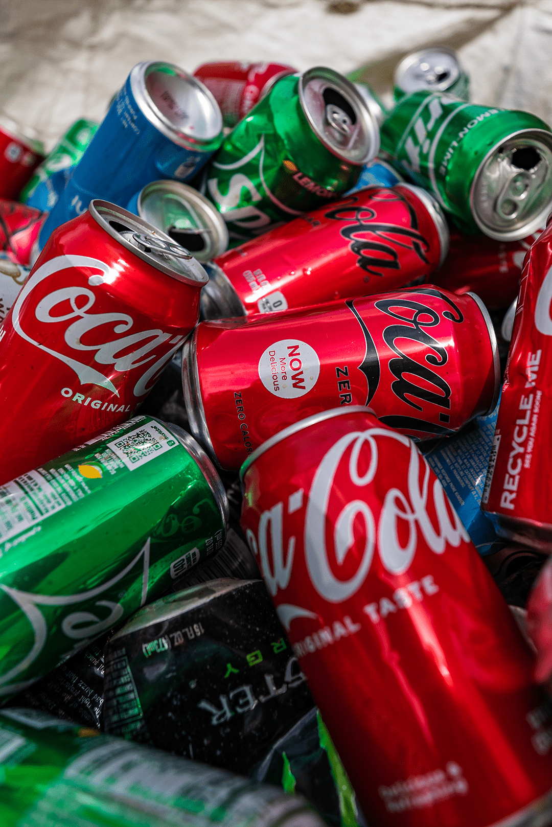 A pile of crumpled and colorful soda cans, including Coca-Cola and Sprite, symbolizing post-consumer waste and the importance of recycling in the beverage industry.