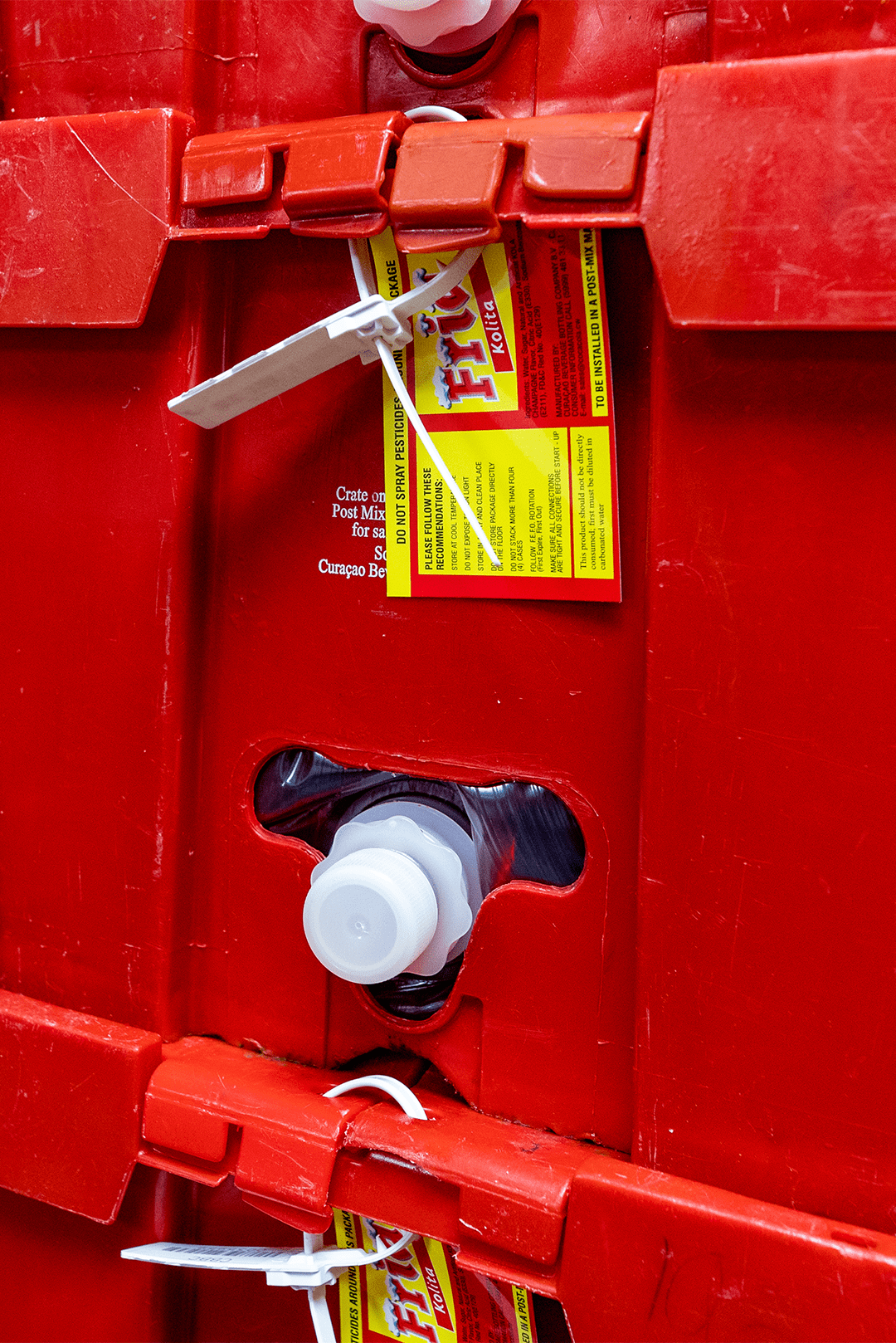 A close-up of a red beverage crate showing secured bottle caps and a tied product label, emphasizing safe packaging and transportation practices in the beverage industry.
