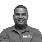 Portrait of Pérez Antonio smiling, wearing a Coca-Cola 80 years commemorative polo shirt, on a white background.